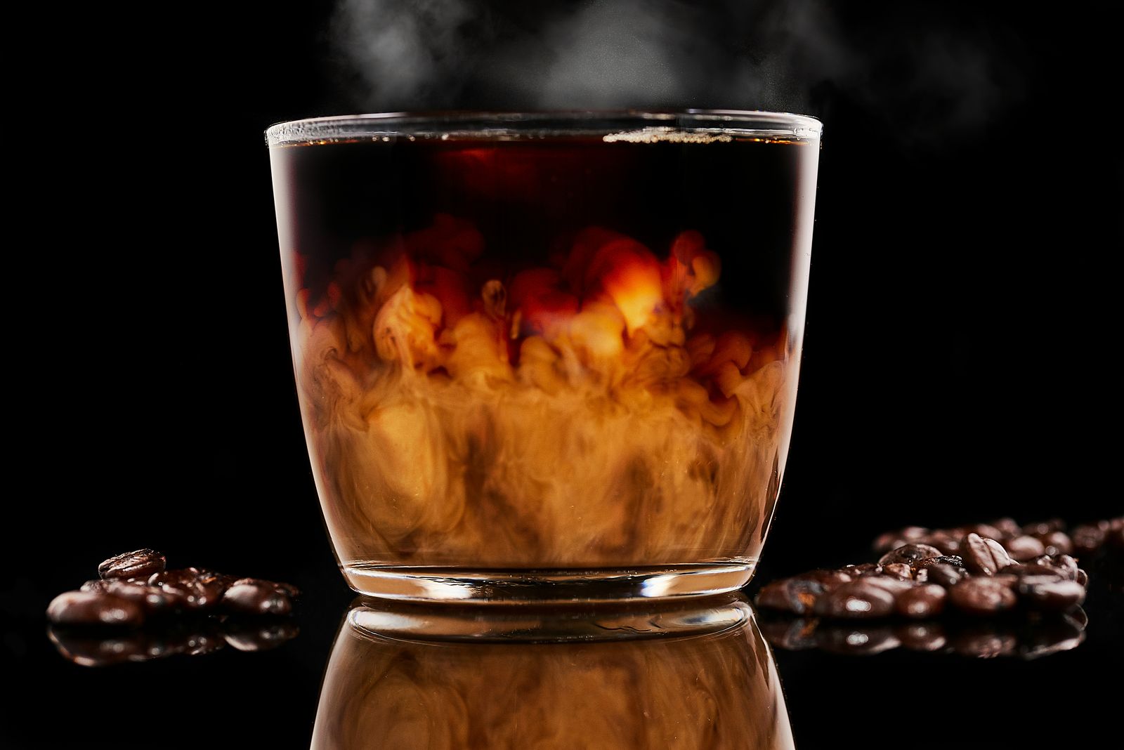 Cream unfurling through a glass of hot coffee on a black surface